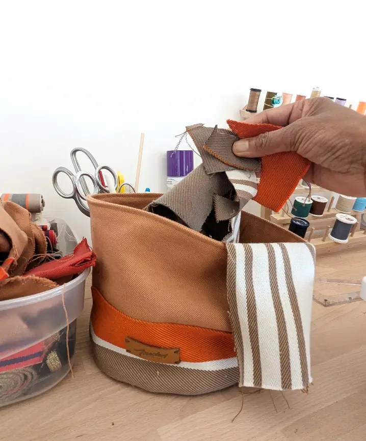 Une main tenant des chutes de tissu au dessus d'une panière en toile basque aux tons orangé posé sur une table