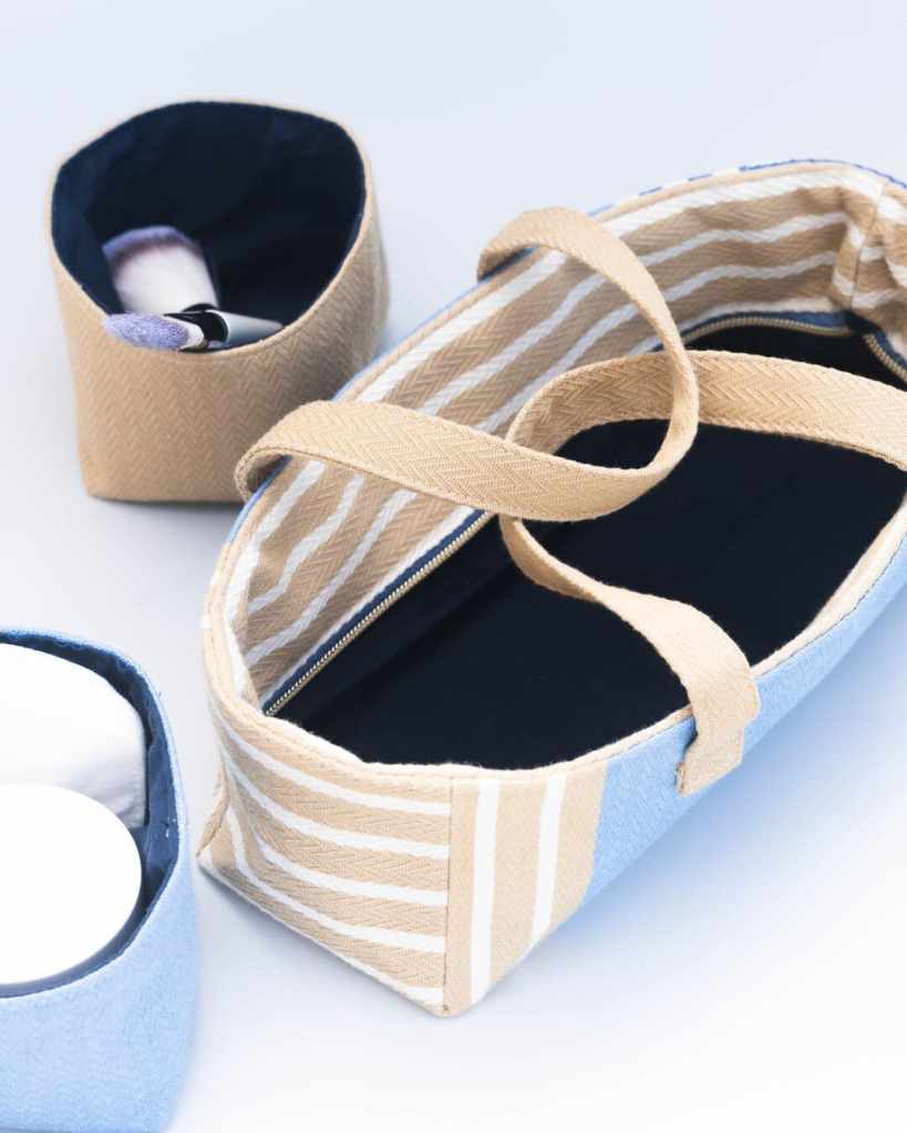 Trousse de toilette raffinée en toile basque avec trois pochons amovibles, affichant un motif chevrons bleu, blanc et beige.